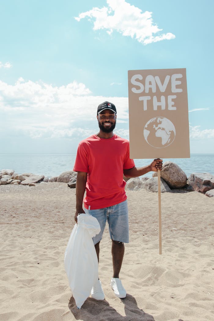 Smiling man with a Save the Planet sign on a sunny beach, promoting environmental awareness.