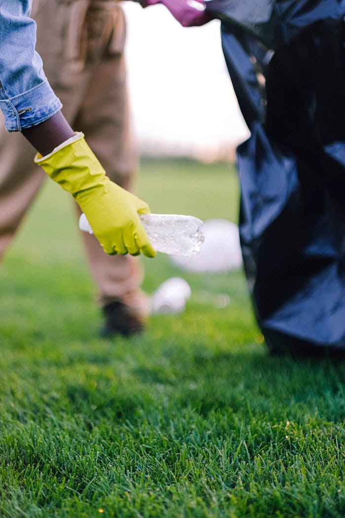Volunteer wearing gloves picks up litter in park, promoting environmental awareness.