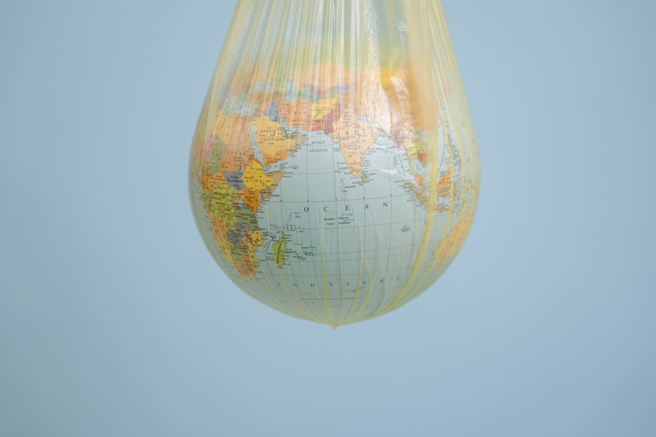 A globe wrapped in a plastic bag illustrating environmental concerns with a blue backdrop.